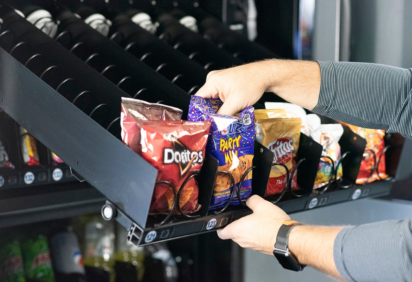 Vending machine with a person selecting chips, including Doritos and Pringles.